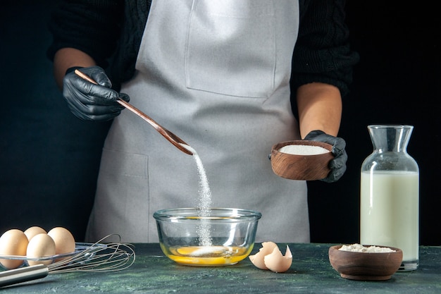 Vista frontal cocinera vertiendo harina en los huevos para la masa en pasteles oscuros pastel pastel trabajador de panadería hotcakes trabajo de cocina