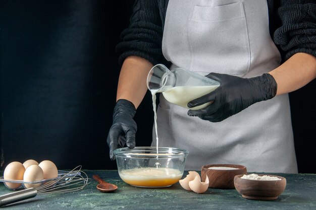 Vista frontal cocinera vertiendo leche en los huevos en pasteles oscuros pastel pastel trabajador cocina masa trabajo hotcakes