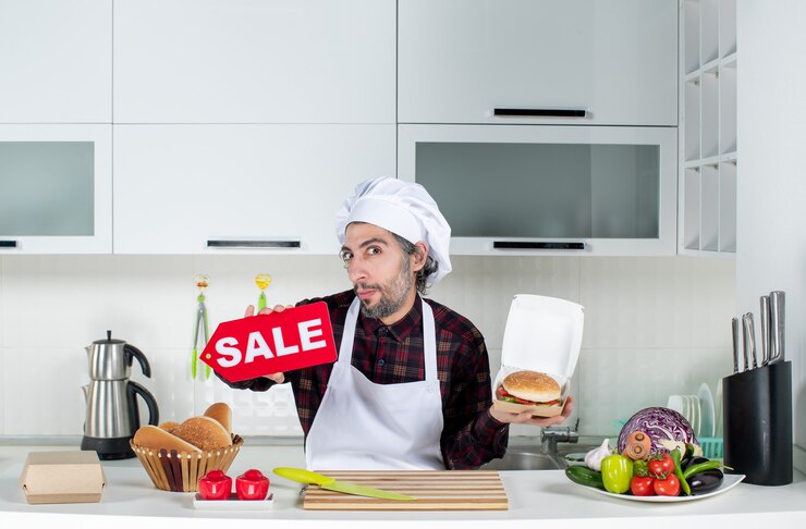 Foto gratuito vista frontal del cocinero macho sosteniendo cartel de venta y hamburguesa en la cocina