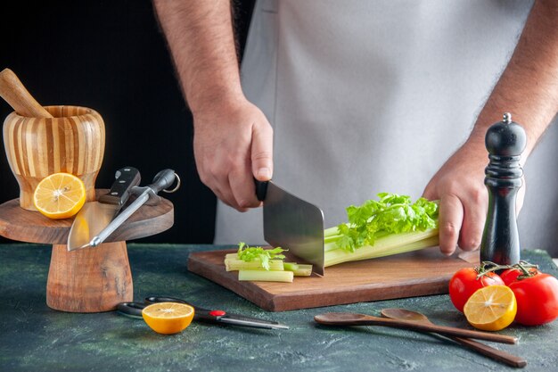 Vista frontal cocinero masculino cortando el apio en una pared oscura comida de dieta ensalada de fotografía en color salud alimentaria