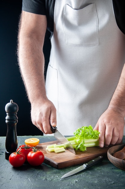Vista frontal del cocinero masculino cortando el apio en la pared oscura, ensalada, dieta, comida, fotografía, salud alimentaria