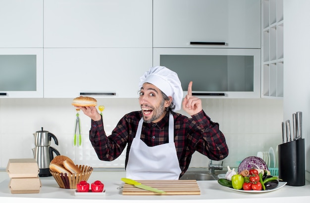 Vista frontal del cocinero masculino sosteniendo pan sorprendente con una idea en la cocina