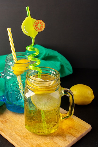 Una vista frontal cóctel de limón bebida fresca fresca dentro de vasos de vidrio en rodajas y limones enteros pajitas de colores sobre el fondo oscuro cóctel bebida fruta