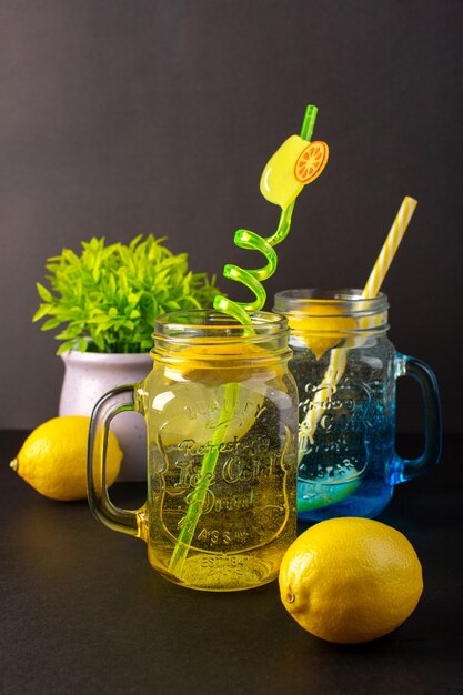 Una vista frontal cóctel de limón bebida fresca fresca dentro de vasos de vidrio en rodajas y pajitas de limones enteros sobre el fondo oscuro cóctel bebida fruta