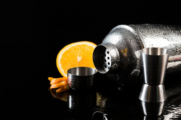 Vista frontal de la coctelera con naranja y vaso de chupito