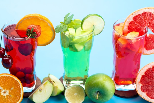 Una vista frontal de cócteles de frutas frescas con rodajas de fruta fresca enfriamiento con hielo en azul, cóctel de jugo de bebida color de fruta