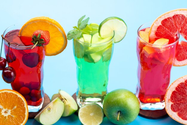 Una vista frontal de cócteles de frutas frescas con rodajas de fruta fresca enfriamiento con hielo en azul, cóctel de jugo de bebida color de fruta