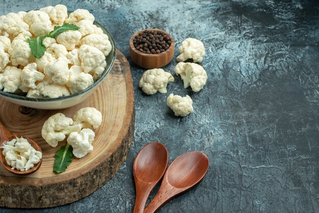 Vista frontal de coliflor fresca con cucharas y pimiento sobre superficie gris claro