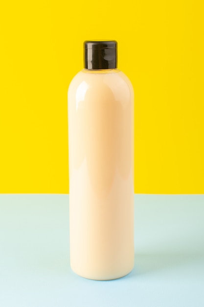 Una vista frontal de color crema botella de champú de plástico puede con tapa negra aislada fondo amarillo-hielo-azul cosméticos belleza cabello