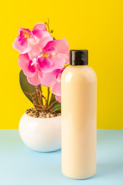 Foto gratuita una vista frontal de color crema botella de champú de plástico puede con tapa negra aislada junto con flores sobre el fondo amarillo-helado-azul cosméticos belleza cabello