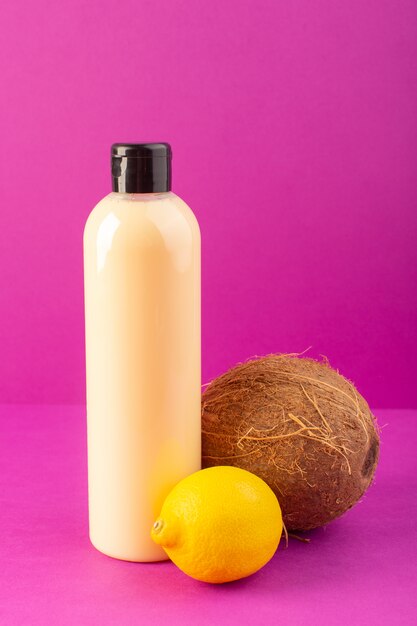 Una vista frontal de color crema botella de champú de plástico puede con tapa negra junto con limones y coco aislado en el fondo púrpura cosméticos belleza cabello