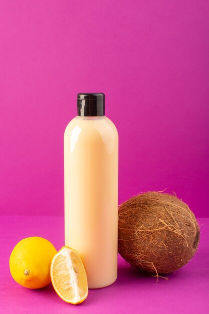 Una vista frontal de color crema botella de champú de plástico puede con tapa negra junto con limones y coco aislado en el fondo púrpura cosméticos belleza cabello