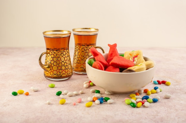 Vista frontal de coloridas deliciosas galletas diferentes formadas dentro de la placa con dulces y tazas de té