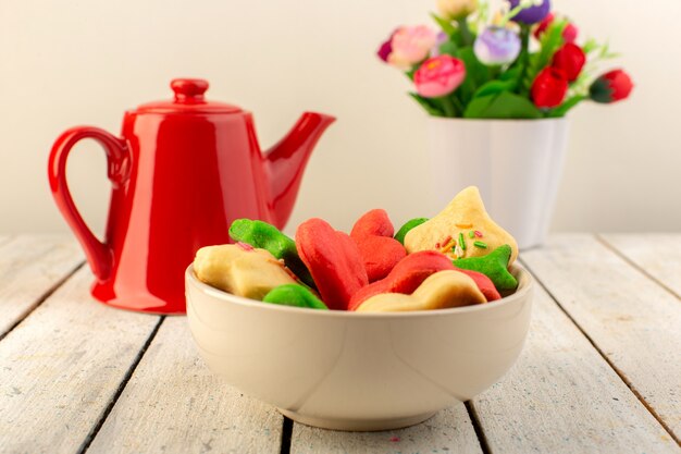 Vista frontal de coloridas deliciosas galletas diferentes formadas dentro de la placa con tetera roja y flores.