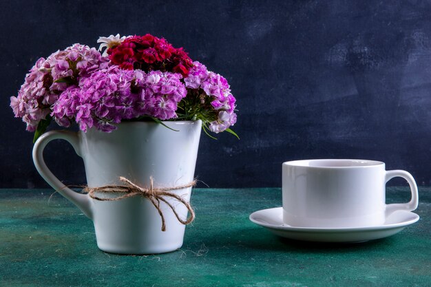 Vista frontal coloridas flores en una taza blanca con una taza de té en el plato