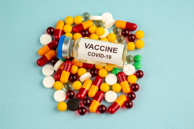 Vista frontal de coloridas píldoras con vacuna en la superficie azul hospital de salud de color covid- laboratorio de ciencias pandemia de virus de drogas