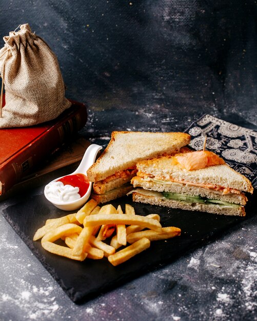 Vista frontal comida escritorio negro con papas fritas y sandwich en el piso gris