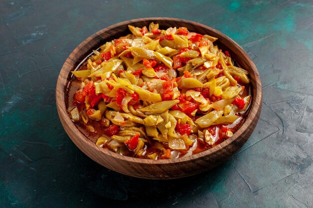 Vista frontal de la comida vegetal en rodajas cocinada con diferentes ingredientes en la superficie azul