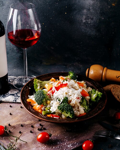 Vista frontal, comida de verduras, vitaminas coloreadas, ricas junto con una botella de vino tinto en el escritorio gris