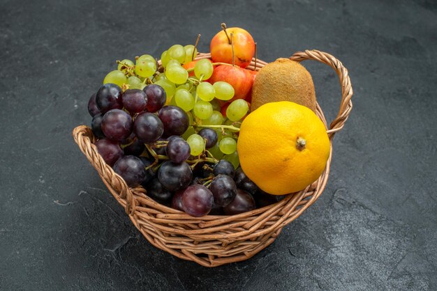 Vista frontal de la composición de diferentes frutas frescas y maduras dentro de la canasta sobre fondo gris oscuro suaves frutas frescas salud madura