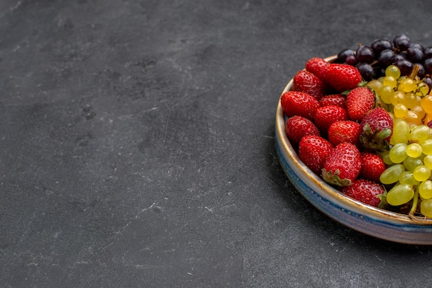 Vista frontal de la composición de la fruta fresas uvas frambuesas y mandarinas en el espacio oscuro