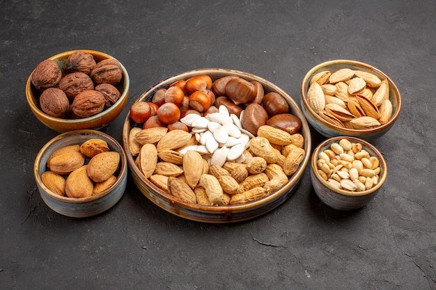 Vista frontal de la composición de nueces cacahuetes y otras nueces sobre una superficie gris oscuro