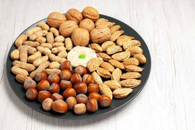 Vista frontal de la composición de nueces nueces frescas maní y avellanas placa interior en blanco escritorio árbol de nueces planta de bocadillos muchos shell