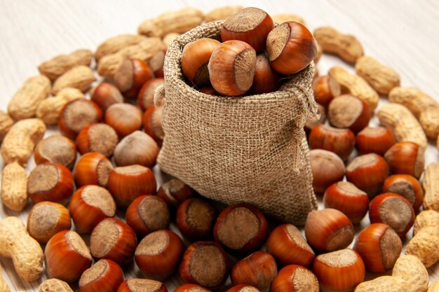 Vista frontal de la composición de la tuerca avellanas frescas y cacahuetes en el escritorio blanco nuez de maní snack nuez