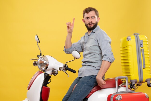 Vista frontal del concepto de viaje con pensamiento joven sentado en motocicleta con maletas apuntando hacia arriba en amarillo