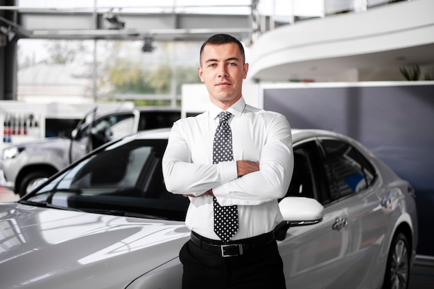 Vista frontal concesionario de automóviles masculinos de pie con los brazos cruzados