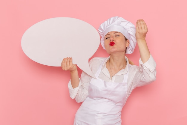 Vista frontal confitería femenina en ropa blanca con cartel blanco en la pared rosa pastelería dulce de confitería