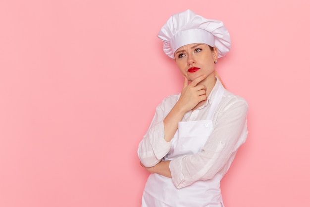 Vista frontal confitería femenina en ropa blanca posando con expresión de pensamiento en el trabajo de trabajo de pastelería dulce confitería de escritorio rosa claro