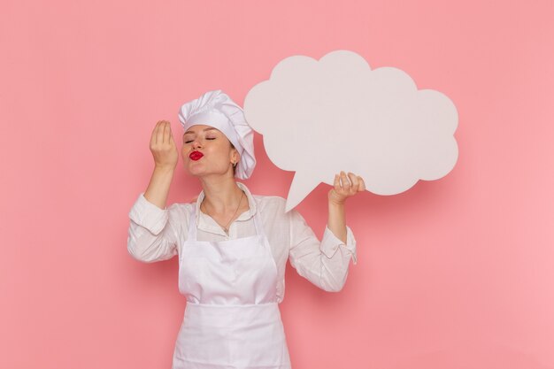 Vista frontal confitero femenino en ropa blanca con gran cartel blanco en la pared rosa cocinar trabajo cocina cocina comida