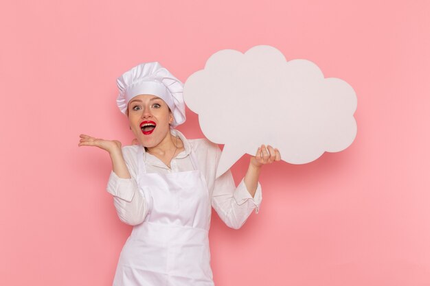 Vista frontal confitero femenino en ropa blanca con gran cartel blanco en la pared rosa cocinar trabajo cocina cocina comida