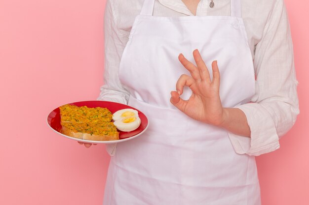 Vista frontal confitero femenino en ropa blanca con plato con tostadas y huevo en la pared rosa cocinar trabajo cocina cocina comida