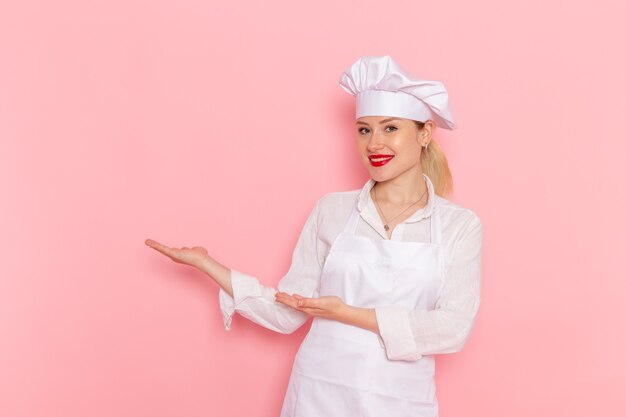 Vista frontal confitero femenino en ropa blanca sonriendo y posando en la pared rosa cocinar confitería trabajo de pastelería dulce