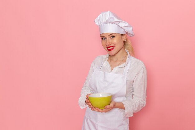 Vista frontal confitero femenino en ropa blanca sosteniendo placa verde en la pared rosa comida comida sopa verduras vegetales