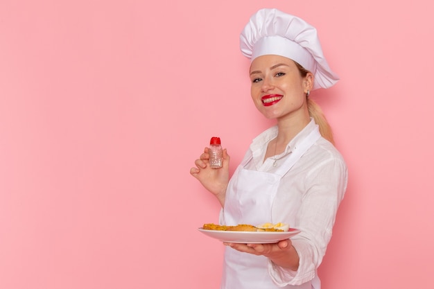 Vista frontal confitero femenino en ropa blanca sosteniendo un plato con comida en la pared rosa cocinar trabajo cocina cocina comida