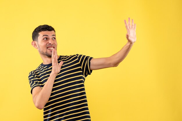 Vista frontal confundido hombre joven en camiseta a rayas blanco y negro fondo amarillo aislado