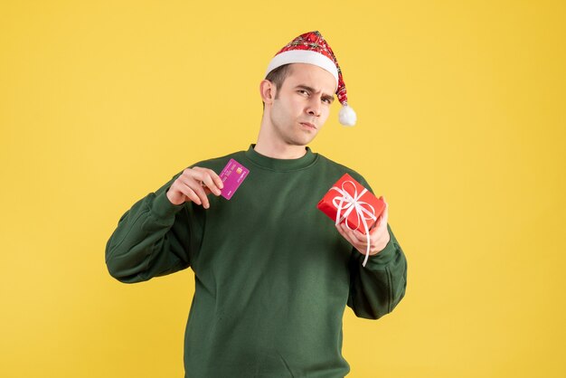 Vista frontal confundido joven con pie de regalo de Navidad en amarillo