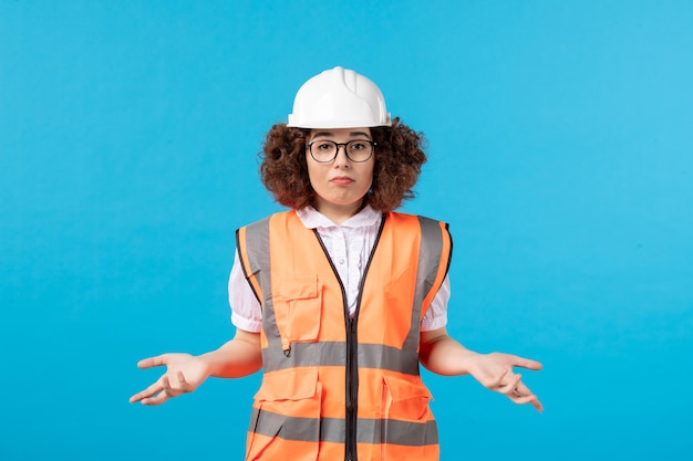 Vista frontal de la confusa trabajadora en uniforme en la pared azul