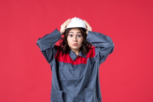 Vista frontal del constructor femenino sorprendido en uniforme con casco sobre fondo rojo aislado