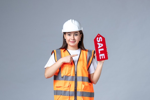 Vista frontal del constructor femenino con tablero de venta rojo sobre pared gris