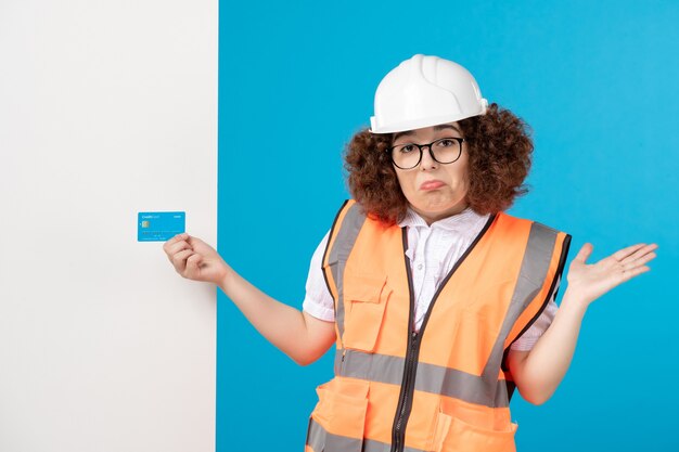 Vista frontal del constructor femenino en uniforme y casco en la pared azul