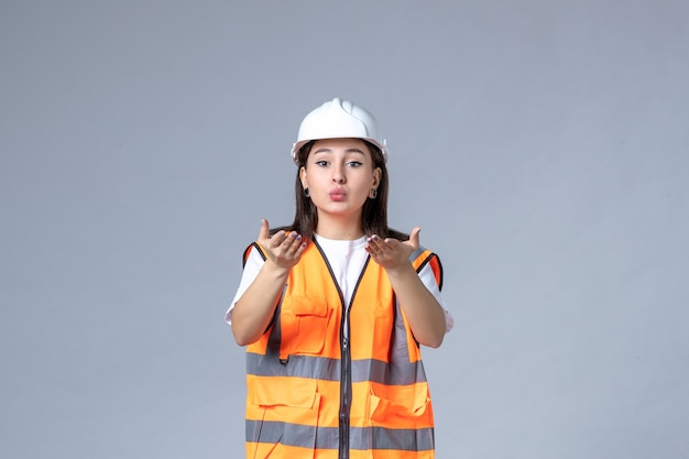 Vista frontal del constructor femenino en uniforme y casco protector en pared gris