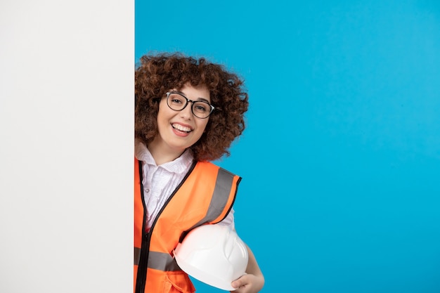 Vista frontal del constructor femenino en uniforme en la pared azul