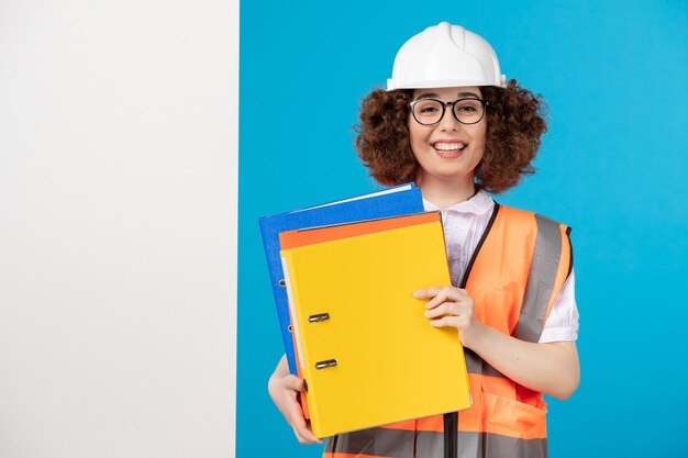 Vista frontal del constructor femenino en uniforme en la pared azul