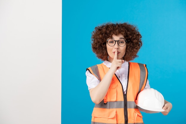 Vista frontal del constructor femenino en uniforme en la pared azul