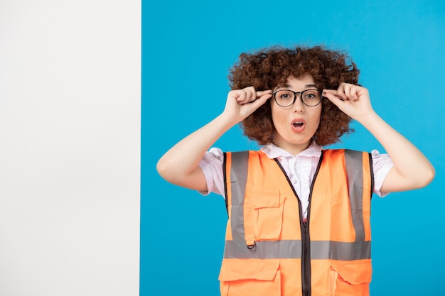 Vista frontal del constructor femenino en uniforme en la pared azul