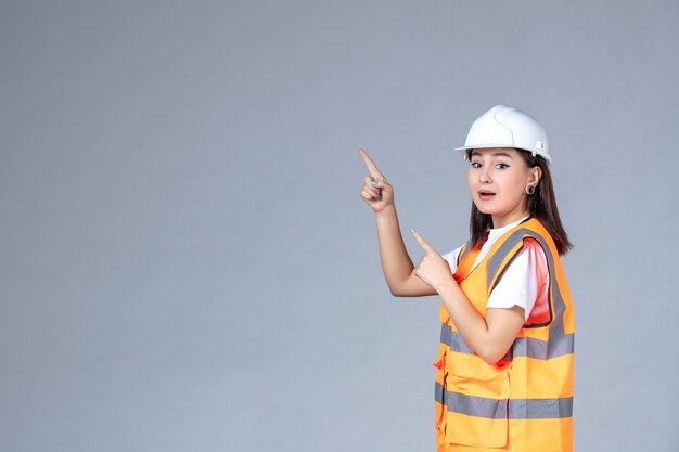 Vista frontal del constructor femenino en uniforme en la pared blanca